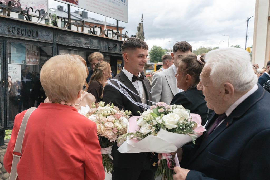 Nowożeńcy przyjmujący gratulacje i kwiaty przed kościołem.