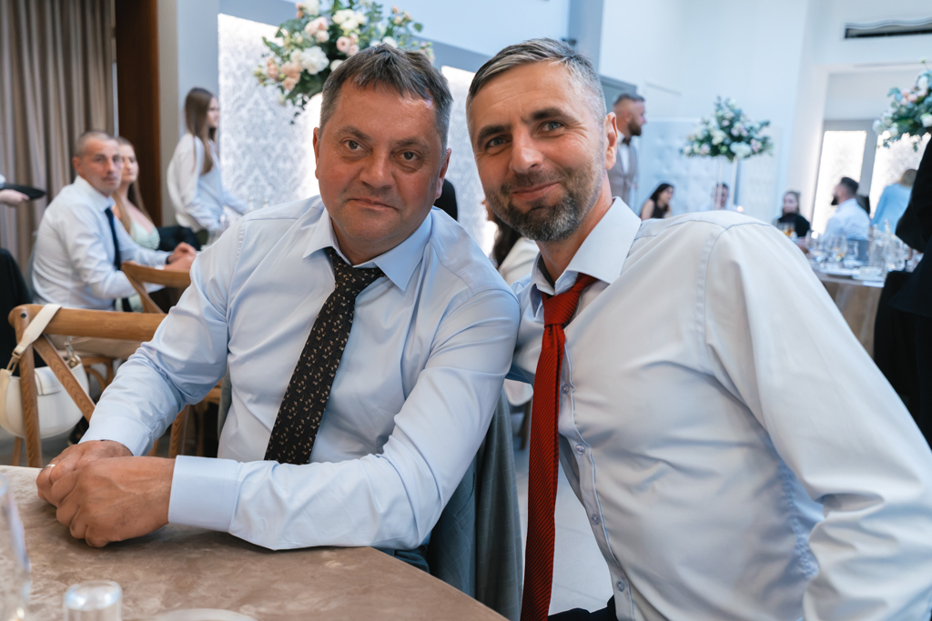 Dwaj mężczyźni pozujący przy stole podczas przyjęcia weselnego.