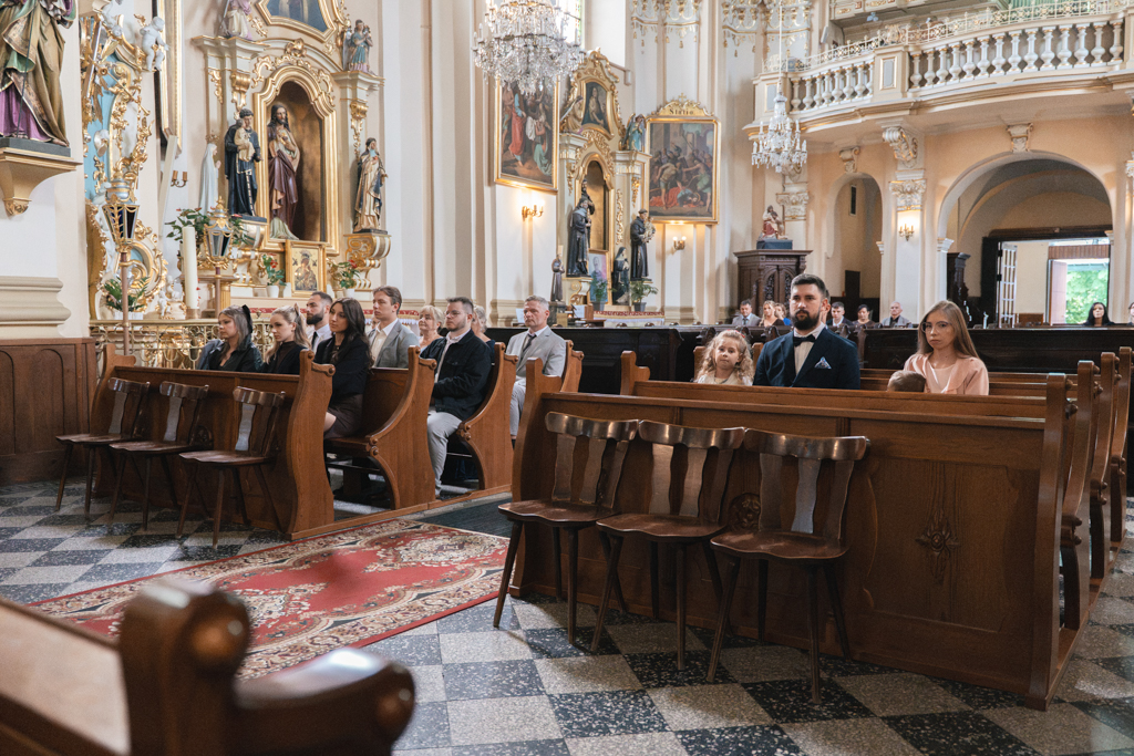 Rodzina i goście ślubni w drewnianych ławkach kościoła.