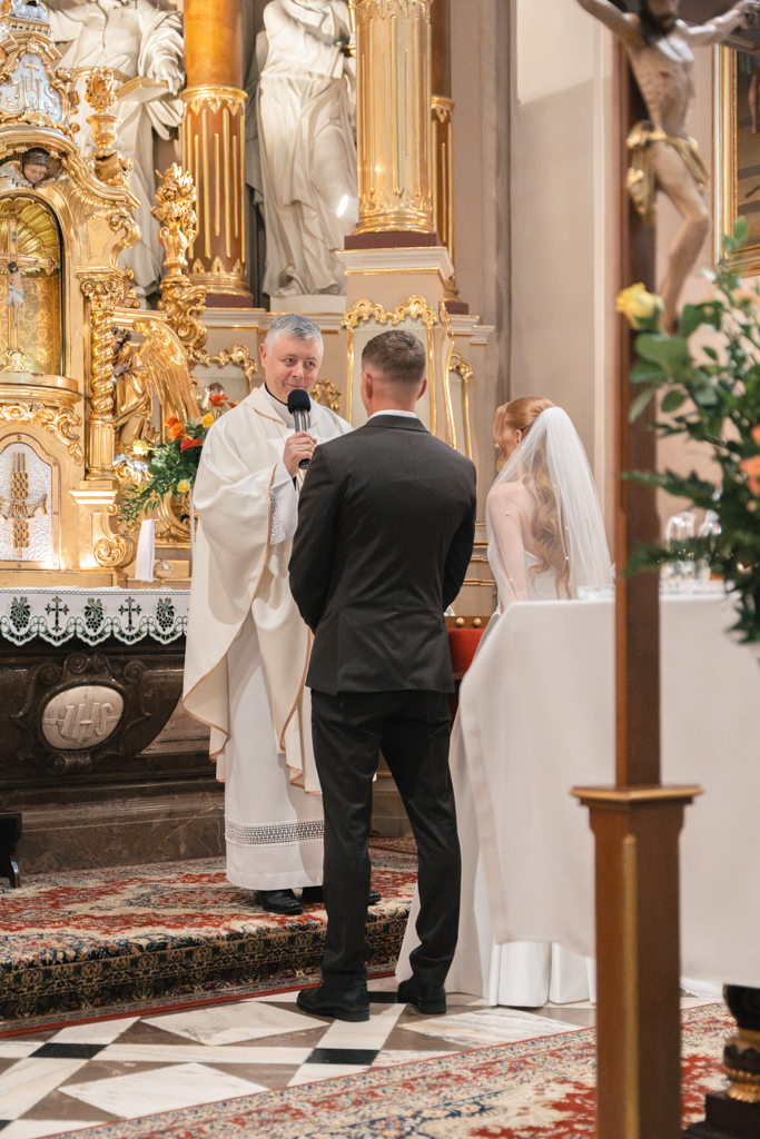 Pan młody i panna młoda stojący przed księdzem w kościele.