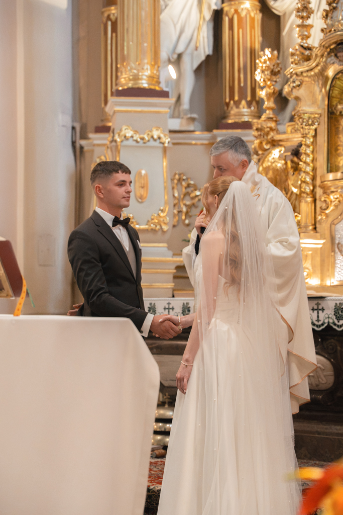 Nowożeńcy i ksiądz przy ołtarzu podczas ceremonii.