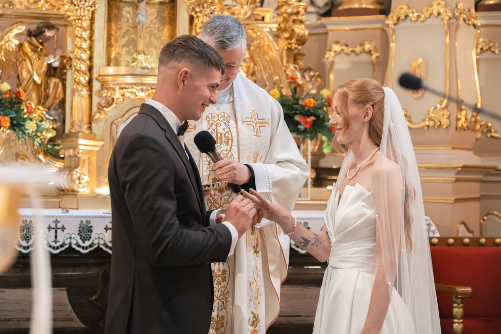 Panna młoda zakładająca obrączkę panu młodemu przy ołtarzu.