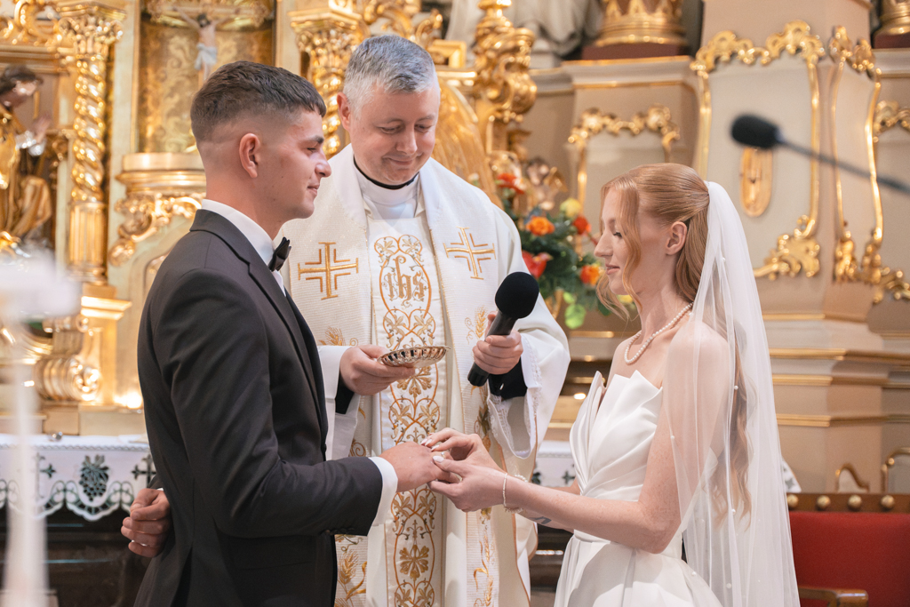 Nowożeńcy wymieniający obrączki w obecności księdza.