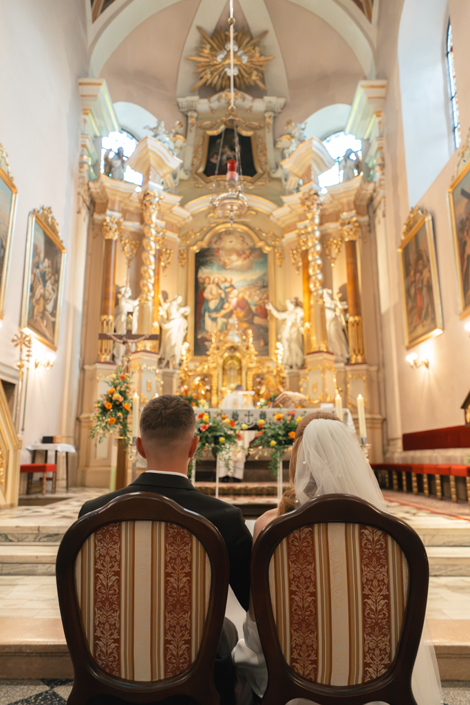 Para młoda siedząca przed ołtarzem podczas ceremonii ślubnej.