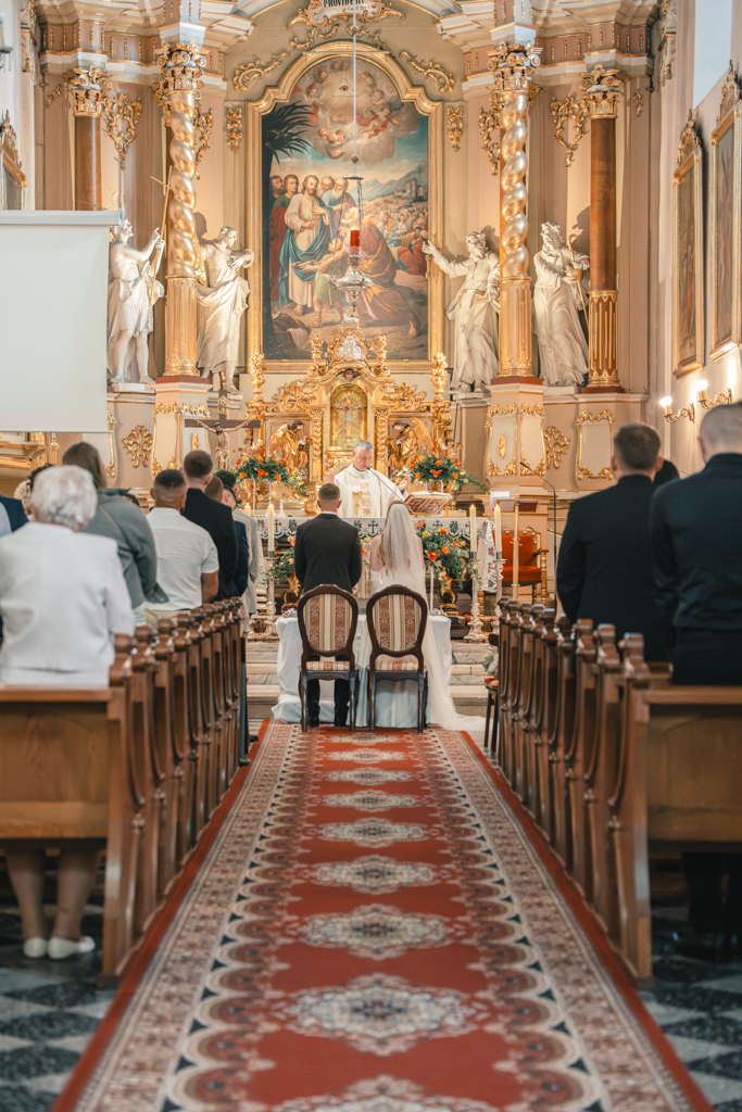 Widok na nawę kościoła i bogato zdobiony ołtarz podczas ślubu.